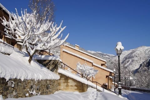 Cozy chalets with warm ochre façades blanketed in fresh mountain snow under a bright blue sky.