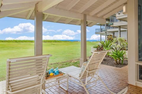 A relaxing covered patio with lounge chairs overlooking a lush green lawn and distant ocean views under a bright blue sky.