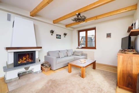 A cozy living area featuring a modern sofa, wooden coffee table, and a fireplace. Large windows offer natural light.