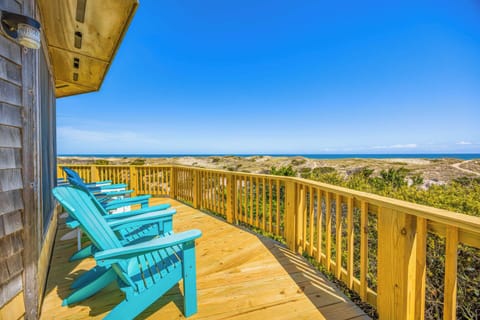 Unwind in your turquoise Adirondack chairs as endless ocean views stretch before you, framed by coastal dunes and vibrant greenery under brilliant blue skies.