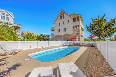 Private outdoor pool surrounded by sunny decks and shaded loungers creates your perfect coastal retreat. The inviting blue water beckons under clear skies.