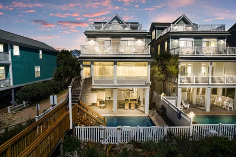 Stunning beachfront property with multiple decks and private pool, surrounded by coastal charm as evening light creates a magical atmosphere.