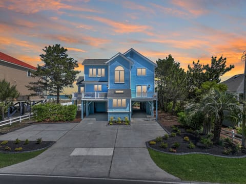 Distinctive blue coastal home with dramatic sunset skies creating a stunning arrival experience in this peaceful neighborhood setting.