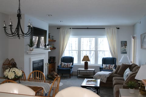 Large comfy living room with big flatscreen TV over wood burning fireplace