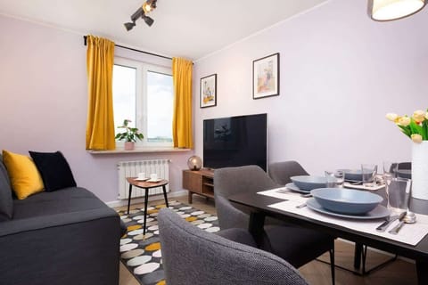 A cozy living room featuring a comfortable gray sofa, bright yellow curtains, and a coffee table with a decorative plant, perfect for relaxation.