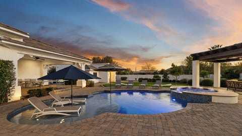 Resort pool and spa with sun shelf, loungers, umbrellas, and sunset glow