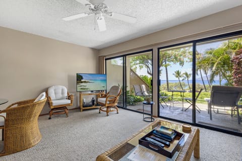 Step into your tropical retreat where ceiling fan breezes meet stunning ocean views through expansive sliding glass doors—your perfect island escape with cozy seating and direct patio access.