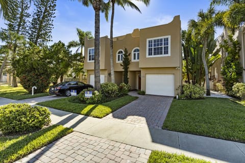 Mediterranean-style two-story home exterior with attached garage, paved driveway, and tropical palm tree landscaping