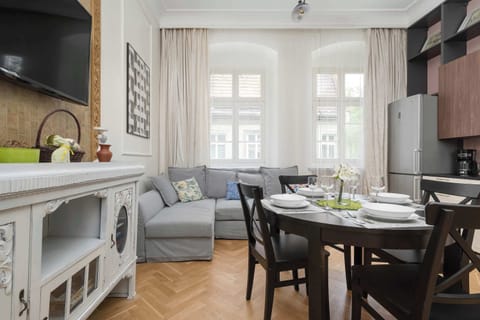 A dining area with a dark wooden table and chairs, placed next to a cozy sitting space and large windows with curtains.