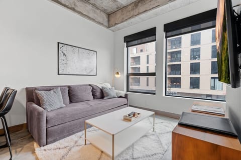 Unwind in your stylish living room with exposed beam ceilings, plush sofa, and city views through large windows.