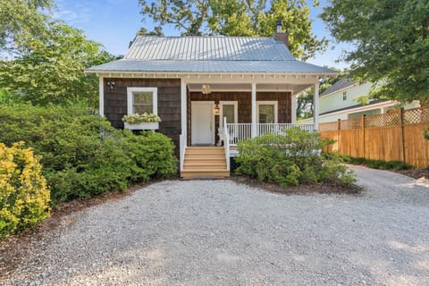 This charming cottage welcomes you with a bright covered porch and lush, mature trees all around. The gravel driveway and tidy landscaping frame a classic, peaceful retreat in a residential neighborhood.