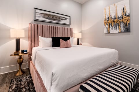 Spacious primary bedroom #1 featuring a king size bed and a designer built in closet. The bedroom is equipped with end tables, lamps, hangers, luggage rack, alarm clock, white noise machine