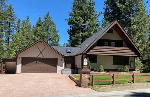 Exterior view of the two-story house with brown garage doors, beige siding, and a brick-paved driveway under a clear blue sky.