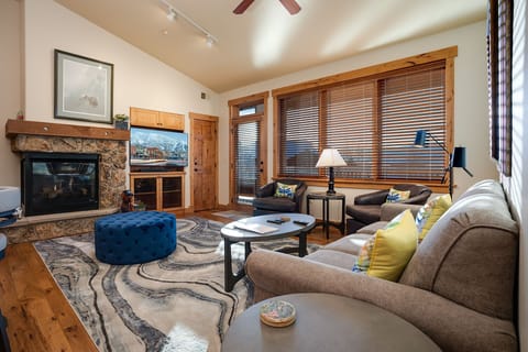 Unwind in your spacious living room with plush seating, a cozy stone fireplace, and warm wood accents creating the perfect mountain retreat atmosphere.