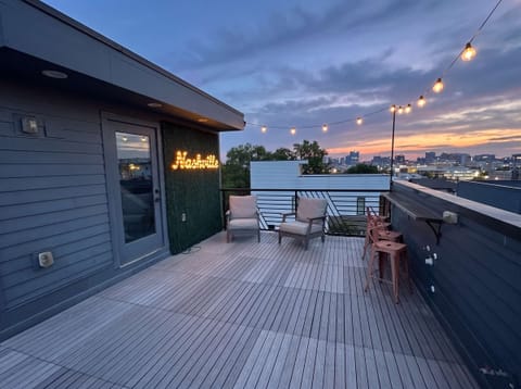 Spacious private rooftop deck with comfortable lounge seating, string lights, and beautiful skyline and sunset views.

