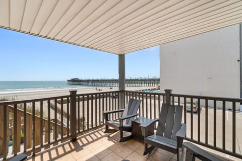 Covered balcony overlooking the beach and fishing pier, offering a shaded retreat with comfortable seating just steps from the shore.