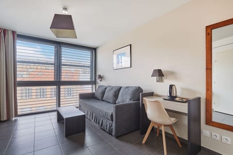 Step into this inviting living space, where modern design meets comfort with a cozy sofa and sleek desk, all bathed in natural light from expansive windows.