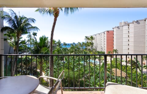 Step onto your private balcony and soak in partial ocean views framed by swaying palms and lush tropical greenery, with nearby resort buildings adding to the vacation ambiance.
