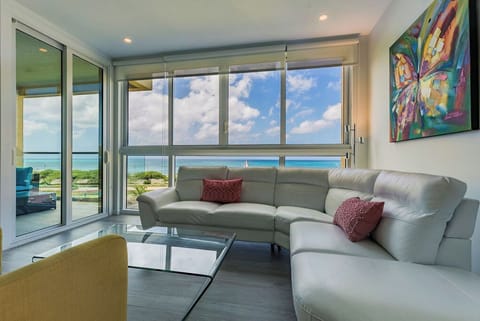 Your spacious living room features modern furnishings, vibrant art, and breathtaking sea views through floor-to-ceiling windows that flood the space with natural light and coastal breezes.