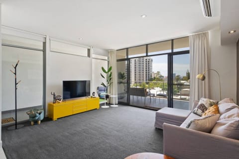 A sunlit living room featuring floor-to-ceiling windows, modern decor, and a pop of colour with a vibrant yellow console.