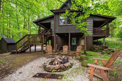 Stone fire pit surrounded by wooden Adirondack chairs sits on gravel beneath the elevated wood cabin deck.