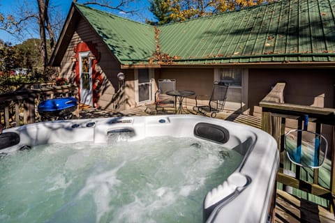 Bubbling white hot tub on wooden deck with black metal chairs and green metal roof backdrop.