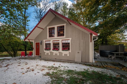 Exterior view of the cottage with taupe siding, red-trimmed windows, flower boxes, and red front door.
