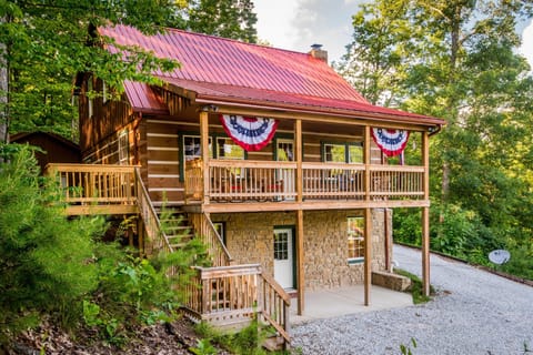 Log cabin exterior with red metal roof, stone lower level, wooden balcony, and patriotic bunting.