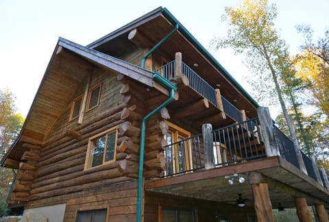 Exterior view of the log cabin’s upper balcony with black metal railings and rustic log posts.