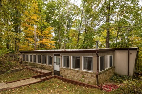 Exterior view of the mobile home shows stone siding below multiple windows and a flat roof surrounded by autumn trees.
