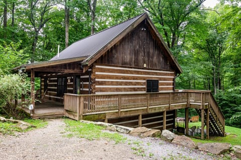 Rustic log cabin exterior with wraparound wooden deck, metal roof, and forest surroundings.