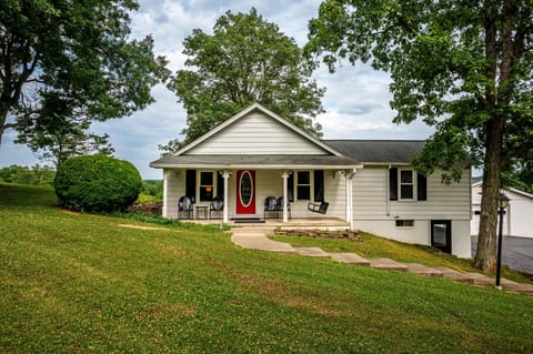 White siding exterior with black shutters, a red oval glass front door, and a covered porch featuring black chairs and a swing.