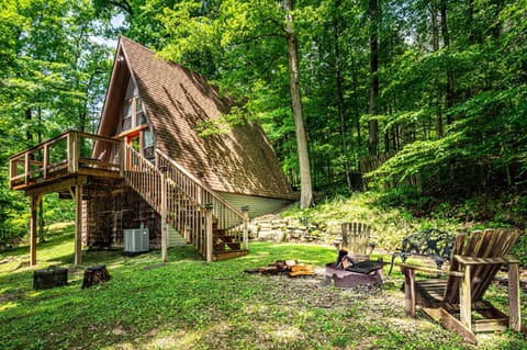 A-frame house with wood-shingled roof and raised deck, surrounded by green trees and a fire pit seating area.