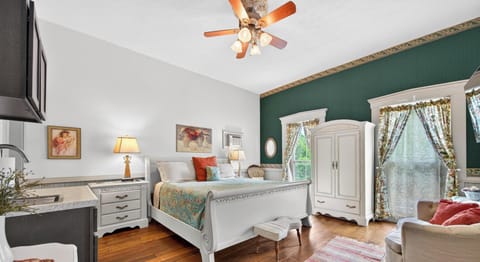 White sleigh bed with floral quilt sits on wide plank hardwood floors beside a striped rug and floral curtains.