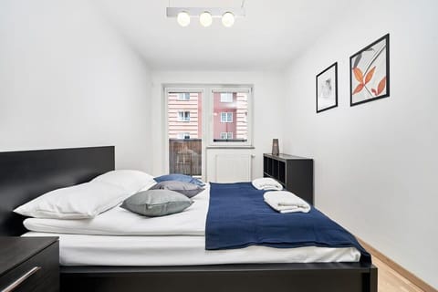 A bedroom with a double bed and two bedside tables. It also has artwork above the bed and large windows allowing natural light to fill the room.