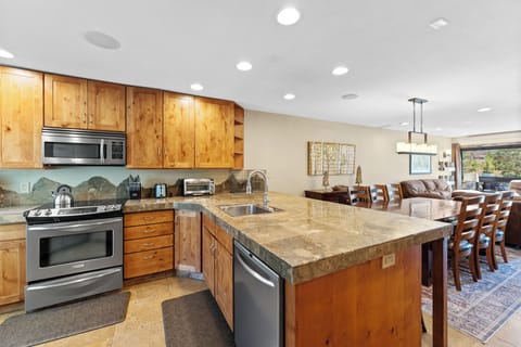Full kitchen with stainless steel appliances, breakfast bar with seating for three, and a wine cooler.