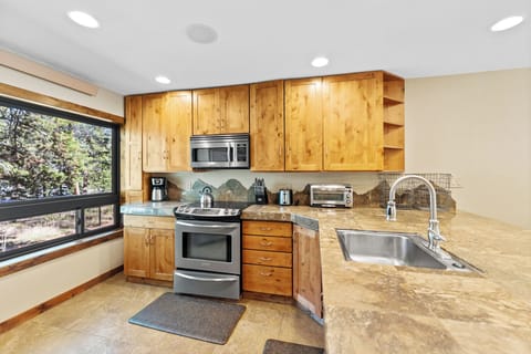 Full kitchen with stainless steel appliances, breakfast bar with seating for three, and a wine cooler.