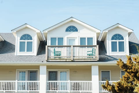 Charming coastal property with multiple balconies and dormers, featuring classic white siding and arched windows in a peaceful residential setting.