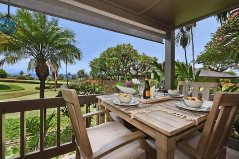 Covered lanai with a four-seat wooden dining set, perfect for enjoying meals or drinks surrounded by lush tropical gardens and distant ocean views.