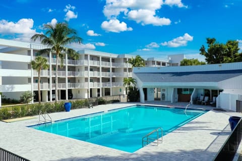 Relaxing heated pool and sun deck - Resort-style heated swimming pool at Island Beach Club Sanibel, surrounded by tropical palms and modern white condos with private balconies under a bright blue Florida sky