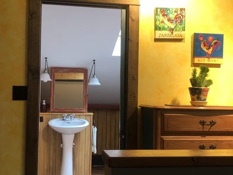 View through a rustic wooden doorway reveals a white pedestal sink, mirror, and hanging lights in the bathroom.