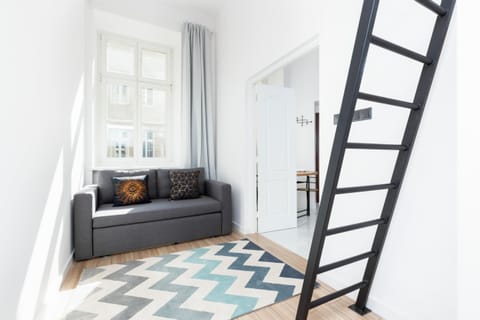 A contemporary, bright living room featuring a black loft ladder, a cozy gray sofa, and a patterned rug. Perfect for small apartments.
