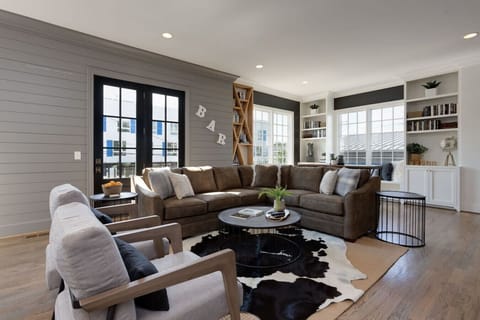 A spacious living room with a large sectional, built-in shelving, and tall windows creates an impressive first impression.
