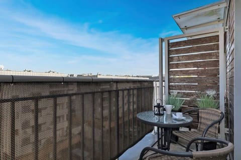 A view from a balcony showing a cityscape or residential area, with outdoor seating and a table with a cup on it.
