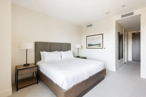 Luxurious king bed, wooden platform bedframe and high suede headboard, white walls and white carpeting, clean mountain decor