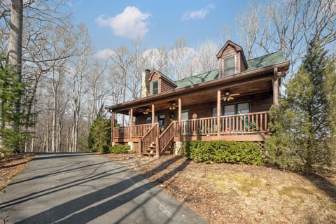 Charming log cabin with wraparound porch nestled among towering trees in a peaceful wooded setting.