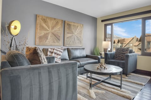 Lowell 304's living room has grey upholstered couch, loveseat, and chair, wood coffee table and white and grey floor rug.