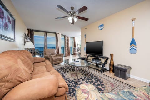 The living area features a cozy brown sofa with queen sleeper, coffee table, and a view of the beach through large windows