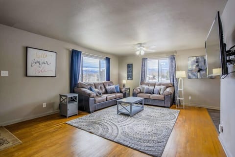 Bright living room with two comfy sofas facing a wall-mounted TV—sprawl out on the patterned rug, set drinks on the glass coffee table, and settle in for a relaxed night together under soft ceiling light.