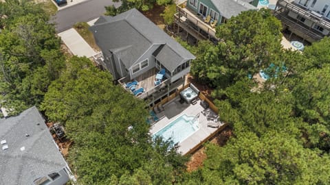 Aerial view of a spacious vacation home nestled among trees, featuring a private pool, hot tub, and large deck—ideal for your coastal getaway.